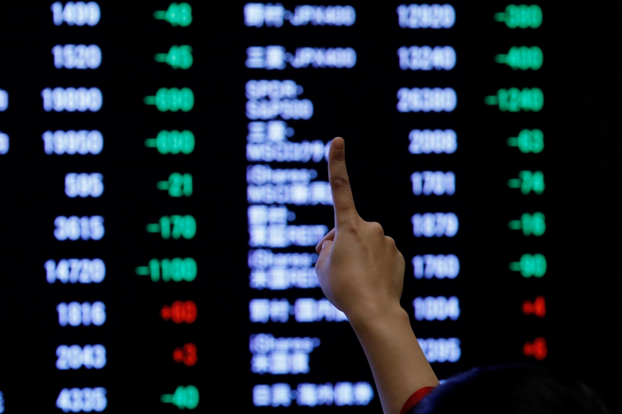 A woman points to an electronic board showing stock prices as she poses in front of the board at the Tokyo Stock Exchange (TSE), in Tokyo, Japan, January 4, 2019. REUTERS/Kim Kyung-Hoon/File Photo