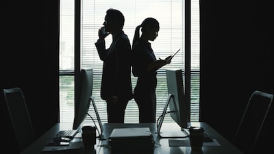 Business couple standing back to back when calling on the phone and reading document