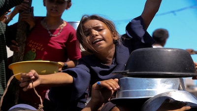 FILE PHOTO: A Palestinian girl gestures as she waits to receive food from a charity kitchen, amid a hunger crisis, in Khan Younis, southern Gaza Strip, August 4, 2025. REUTERS/Hatem Khaled REFILE - QUALITY REPEAT/File Photo