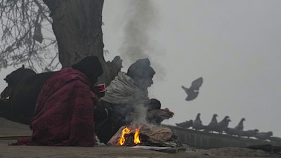 New Delhi: People warm themselves around a small fire on a foggy winter morning, in New Delhi, Saturday, Dec. 20, 2025. Visibility plunged across parts of Delhi on Saturday morning, with buildings and flyovers fading into a grey blur amid dense fog, as the capitals AQI edged closer to the severe  category at 384. (PTI Photo/Kamal Kishore) (PTI12_20_2025_000018B)