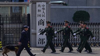 FILE - Paramilitary soldiers and a police officer with a sniffer dog march past the main entrance gate of China's Ministry of Commerce, in Beijing, on April 3, 2025. (AP Photo/Andy Wong, File)