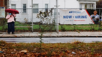 A woman waits for a bus next to a "Now Hiring" sign from the United States Postal Service in Boston, Massachusetts, U.S., October 30, 2021.   REUTERS/Brian Snyder