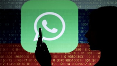 A woman poses for a photo while holding a smartphone in front of a screen showing U.S. messenger app WhatsApp against the backdrop of numerical codes on the state flag of Russia, in this illustration taken February 12, 2026. REUTERS/Ramil Sitdikov/Illustration