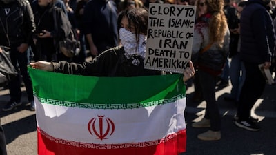 A protester holds an Iranian flag and a placard during an anti-war demonstration towards the U.S. and Israeli embassies following strikes on Iran, in Athens, Greece, March 1, 2026. REUTERS/Stelios Misinas