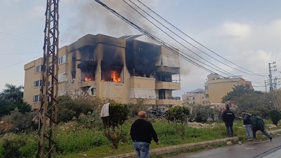 Flames and smoke rise from an apartment building hit by an Israeli airstrike as people gather nearby in the southern port city of Sidon, Lebanon, Saturday, March 14, 2026. AP/PTI(AP03_14_2026_000114B)