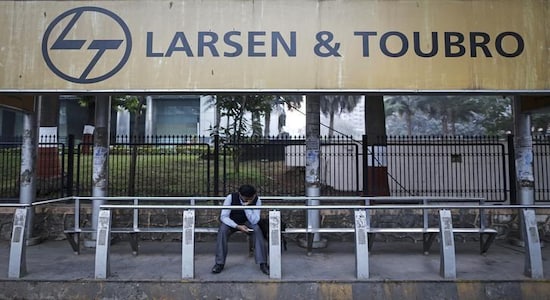 A man waits at a bus-stop with an advertisement of Larsen &amp; Toubro outside the company's manufacturing unit in Mumbai