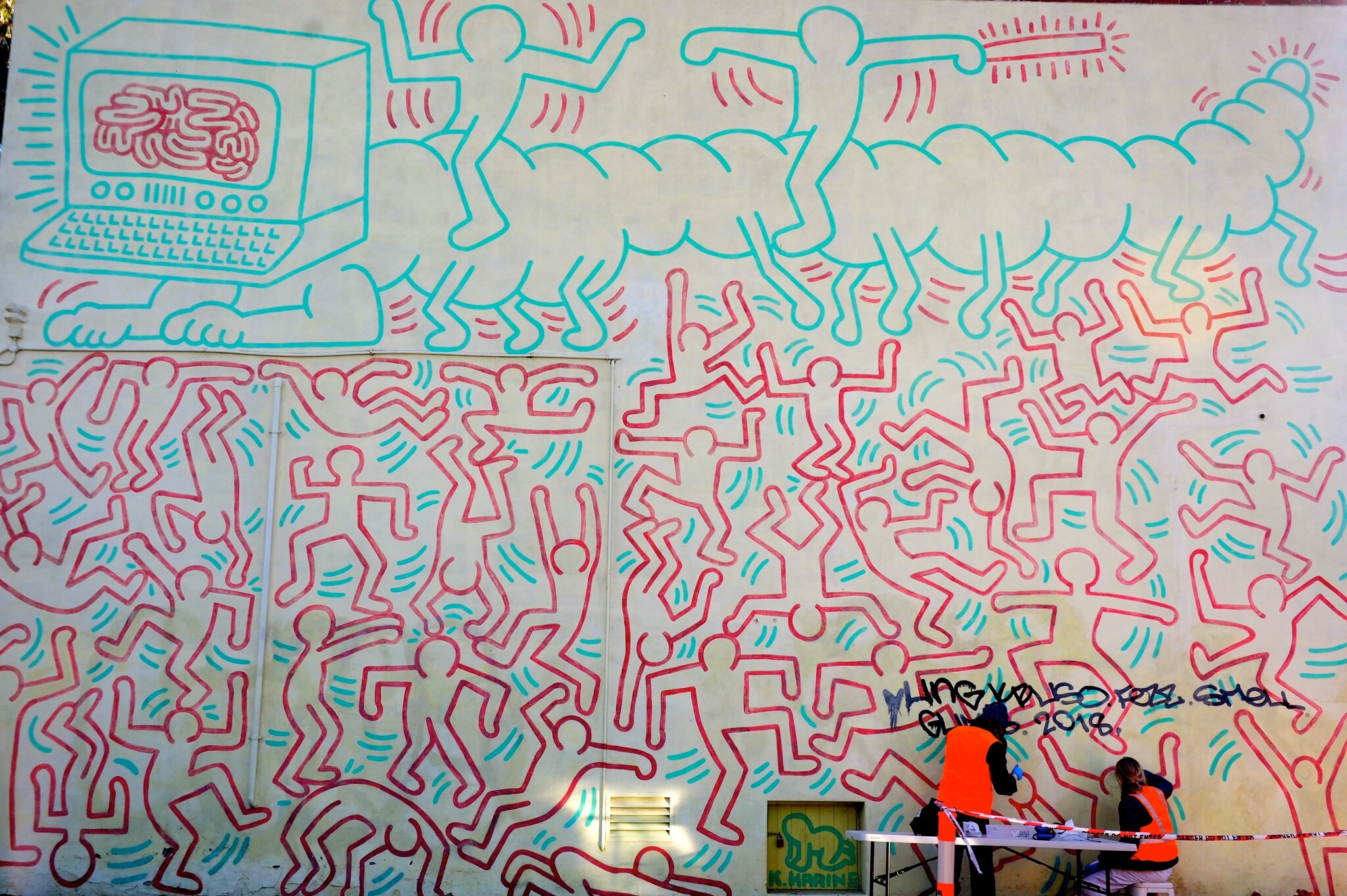 Keith Haring Mural: Located at Johnston Street in Collingwood and painted in 1984 by New York-based artist Keith Haring (1958-1990), this is the oldest and most significant street art mural in Melbourne. It was restored in 2013 and is now listed in the Victoria Heritage Register. In 1984, Haring was commissioned by the National Gallery of Victoria and the Australian Centre for Contemporary Art to create a mural in Melbourne which temporarily replaced the water curtain at the National Gallery. In the photograph, art conservationists can be seen restoring the mural after it was defiled again recently. 