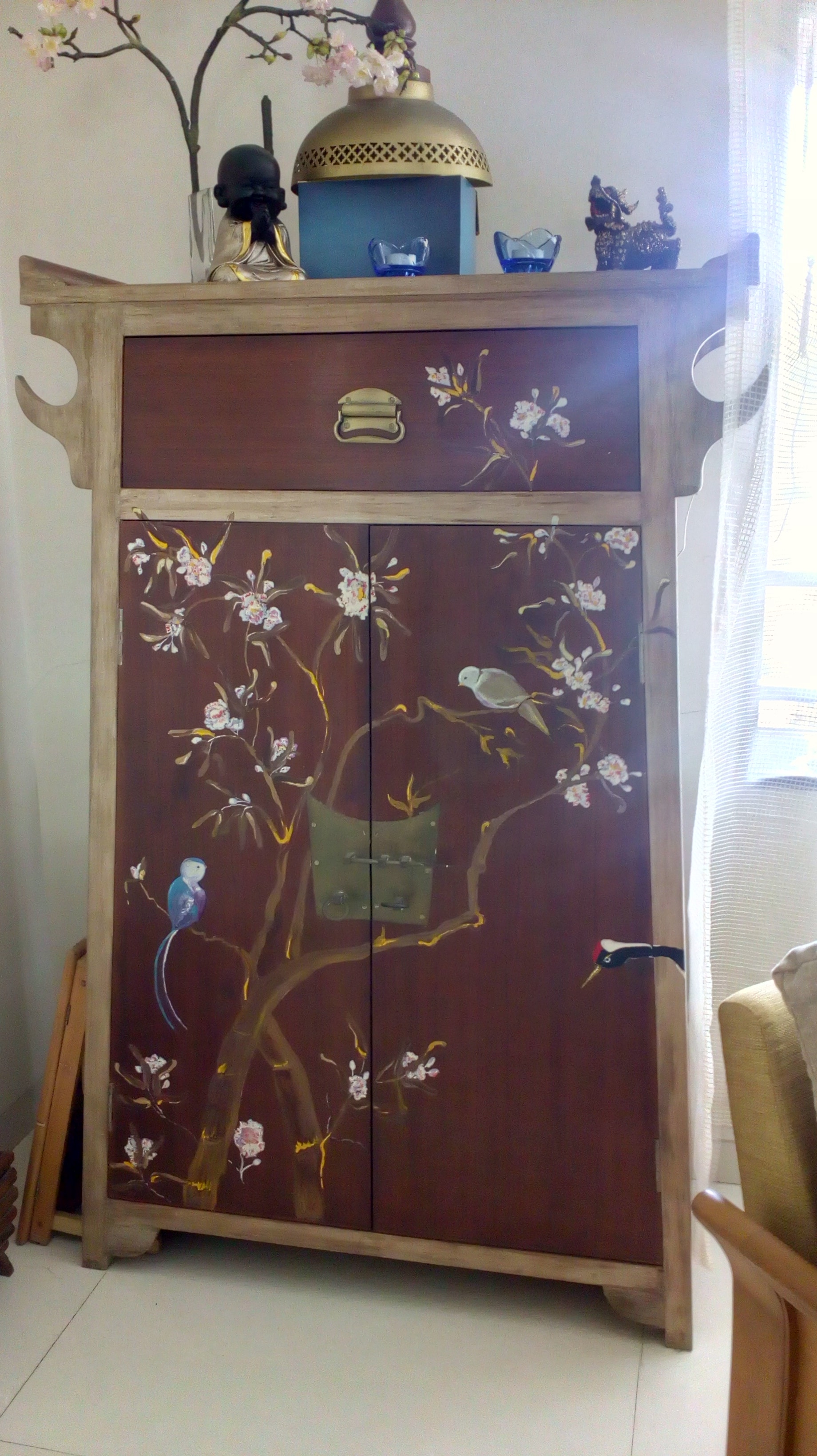 A cabinet with fly eave-looking edges is painted with the cherry blossom tree and birds perched on its branches.