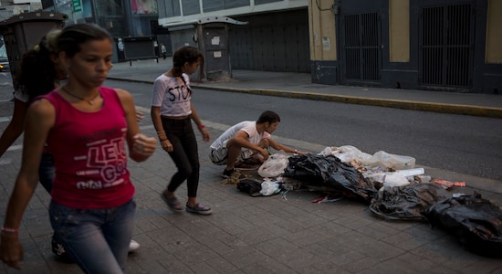 In this Tuesday, July 16, 2019 photo, Kevin Gonzalez searches for food in the trash, on a sidewalk in Caracas, Venezuela. (AP Photo/Rodrigo Abd)