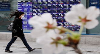 Cherry blossoms bloom in front of a stock quotation board outside a brokerage in Tokyo