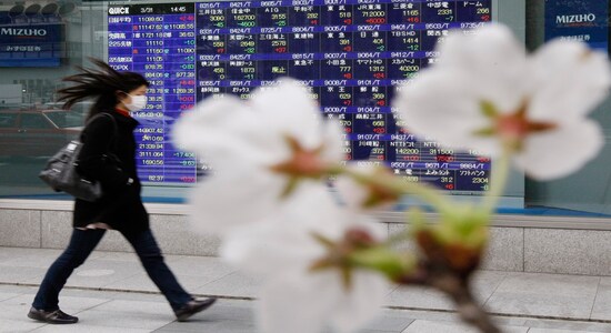 Cherry blossoms bloom in front of a stock quotation board outside a brokerage in Tokyo