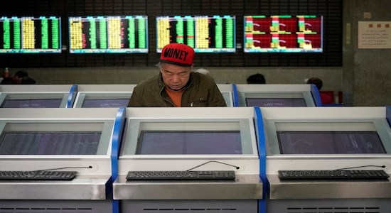 An investor looks at computer screens showing stock information at a brokerage house in Shanghai