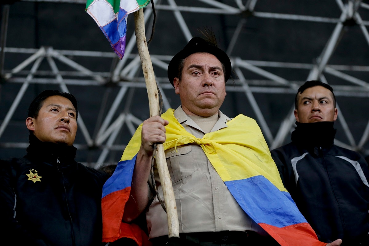 Col. Cristian Rueda Ramos, one of several police officers who has been detained by anti-governments protesters, is made to hold an indigenous banner, don a national flag as a cape and a fedora-styled hat, while presented on a stage at the Casa de Cultura in Quito, Ecuador. Anti-government protesters paraded captive police officers on a stage, defying authorities who are seeking dialogue with opponents, particularly indigenous groups, after deadly unrest that was triggered by fuel price hikes. (AP Photo/Fernando Vergara)