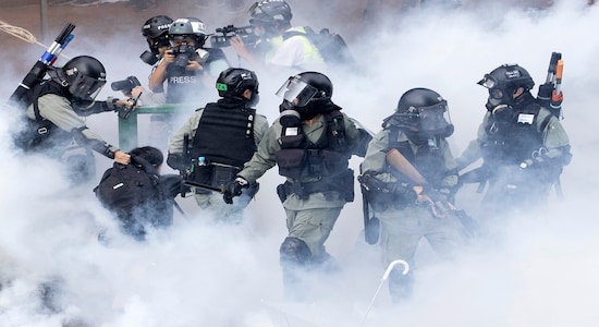 In this Monday, Nov. 18, 2019, file photo, police in riot gear move through a cloud of smoke as they detain a protester at the Hong Kong Polytechnic University in Hong Kong. Hong Kong police fought off protesters with tear gas and batons Monday as they tried to break through a police cordon that is trapping hundreds of them on a university campus. (AP Photo/Ng Han Guan, File)