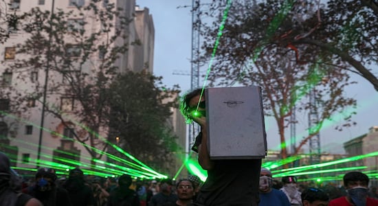 In this Thursday, Nov. 14, 2019 photo, anti-government demonstrators shine laser pointers a the police during a protest in Santiago, Chile. Students in Chile began protesting nearly a month ago over a subway fare hike. The demonstrations have morphed into a massive protest movement demanding improvements in basic services and benefits, including pensions, health, and education. (AP Photo/Esteban Felix)