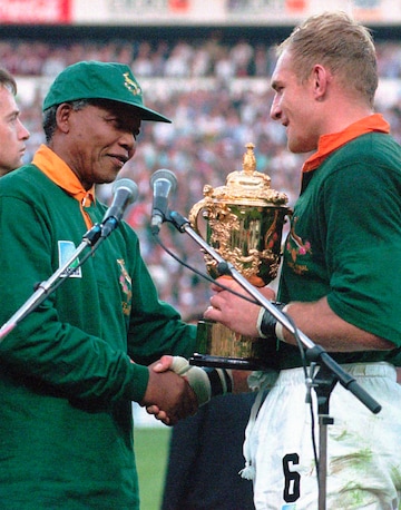 FILE - In this June 24, 1995 file photo, South African rugby captain Francios Pienaar, right, receives the Rugby World Cup from President Nelson Mandela after they defeated New Zealand 15-12 in the final at Ellis Park, Johannesberg, South Africa. Siya Kolisi was a 4-year-old child when South Africa won its first Rugby World Cup title in 1995 but he remembers the national euphoria of the Springboks' second World Cup title in 2007. The first black player appointed as Springboks captain gets his chance at history when he leads South Africa against England in the final on Saturday, Nov. 2, 2019 in Yokohama Japan. (AP Photo/Ross Setford,File)