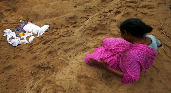 FILE PHOTO: An Indian woman mourns the death of her relatives (covered in white sheets), who were killed when a tsunami hit on Sunday, at a burial ground in Cuddalore, south of the southern Indian city of Madras December 27, 2004. REUTERS/Arko Datta