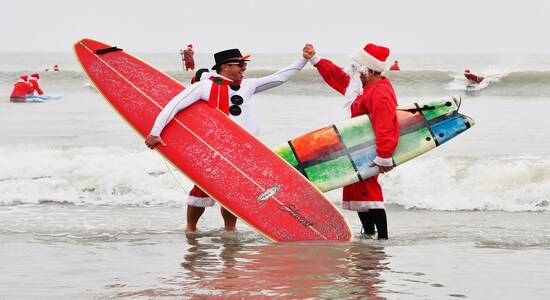 George Trosset Jr. and George Trosset, who started surfing in Santa and Christmas costumes ten years ago behind their house on Christmas Eve, high five each other during the 10th annual Surfing Santas event in Cocoa Beach, Fla., Tuesday, Dec. 24, 2019. The event has grown and now raises money for two local non profits - Grind for Life, which helps with financial assistance for cancer patients, and the Florida Surf Museum. (Malcolm Denemark/Florida Today via AP)