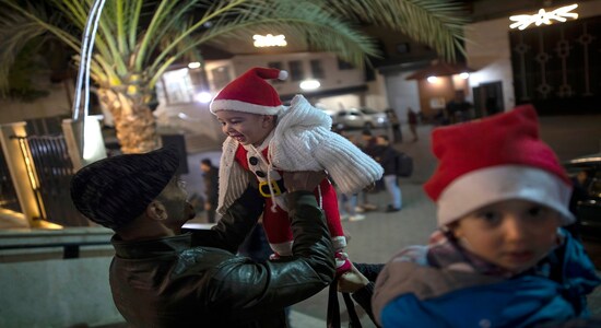 A Palestinian Christian man plays with his baby as they wait for the Christmas Mass outside the Holy Family Catholic Church in Gaza City, Tuesday, Dec. 24, 2019. (AP Photo/ Khalil Hamra)