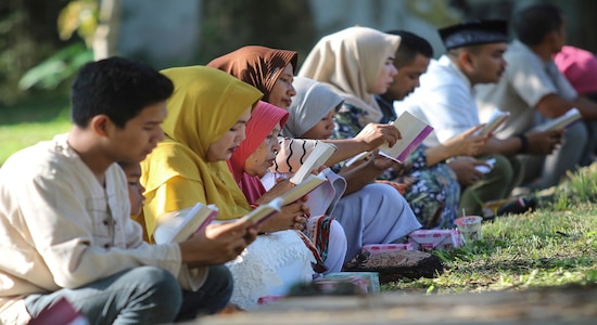 In this Thursday, Dec. 26, 2019, file photo, people read the holy book of the Quran as they pray at a mass grave site for the victims of the Indian Ocean tsunami, during the commemoration of the 15th anniversary of the disaster in Banda Aceh, Indonesia. (AP Photo/Nurhasanah, File)
