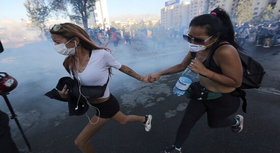 Anti-government demonstrators run away from a cloud of teargas during clashes with the police in Santiago, Chile, Friday, December 20, 2019. Chile is a celebrating second full month of unprecedented social revolt that has not only altered the country's political landscape, but has also pushed a referendum on the reform of the country's dictatorship. (AP Photo/Fernando Llano)