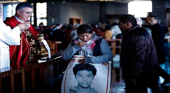 The Bishop of Chilpancingo, Guerrero state, Salvador Rengel, receives the family members of 43 missing students from the Isidro Burgos rural teachers college, carrying posters of their missing loved ones, during Mass at the Basilica of Guadalupe in Mexico City, Thursday, Dec. 26, 2019. Family members continue to call for justice five years after the Ayotzinapa students were allegedly taken from buses by local police and turned over to a drug gang. (AP Photo/Marco Ugarte)