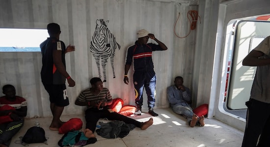 In this Sept. 8, 2019 photo, migrants rescued at sea by the NGOs SOS Mediterranée and Doctors Without Borders rest in the men's shelter aboard the Ocean Viking humanitarian ship as it sails in the Mediterranean Sea. The misery of migrants in Libya has spawned a thriving and lucrative business, in part funded by the EU and enabled by the United Nations, an Associated Press investigation has found. (AP Photo/Renata Brito)