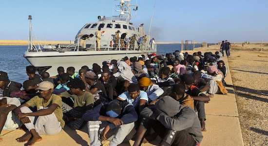 FILE - In this Tuesday, Oct. 1, 2019 file photo, rescued migrants are seated next to a coast guard boat in the city of Khoms, Libya, around 120 kilometers (75 miles) east of Tripoli. When millions of euros started flowing from the European Union into Libya to slow the tide of migrants crossing the Mediterranean, the money came with EU promises to improve detention centers notorious for abuse and to stop human trafficking. That hasn’t happened. (AP Photo/Hazem Ahmed,File)