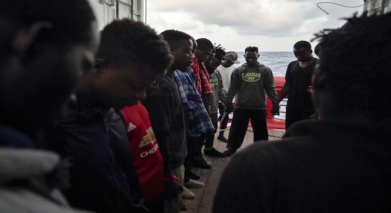 In this Sept. 21, 2019 photo, Eric Boakye, background center wearing a hoodie sweatshirt, and other rescued migrants pray for Europe to grant them a place of safety as they wait aboard the Ocean Viking humanitarian ship in the Mediterranean Sea. Boakye, a Ghanian, was locked in the al-Nasr Martyrs center in Libya twice, both times after he was intercepted at sea. The first time, his jailers simply took the money on him and set him free. He tried again to cross and was again picked up by the coast guard and returned to his jailers.(AP Photo/Renata Brito)