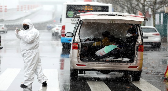 A worker in protective suit stands amid snow to help transport novel coronavirus patients outside a hospital, in Wuhan, Hubei province, China February 15, 2020. China Daily via REUTERS