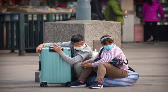 Travelers wearing face masks sit with their luggage outside the Beijing Railway Station in Beijing, Wednesday, March 25, 2020. Some train stations and bus services reopened in China's Hubei Province on Wednesday and people who passed a health check would finally be allowed to travel for the first time since the coronavirus outbreak surged in January. The new coronavirus causes mild or moderate symptoms for most people, but for some, especially older adults and people with existing health problems, it can cause more severe illness or death. (AP Photo/Mark Schiefelbein)