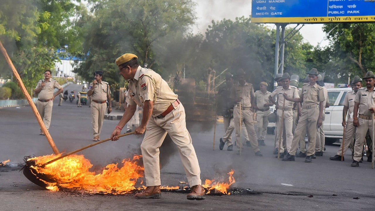 Police personnel try to douse tyres, lit on fire by members of Vishva Hindu Parishad (VHP) during their protest against the killing of tailor Kanhaiya Lal in Udaipur, in Jodhpur. (Image: PTI)
