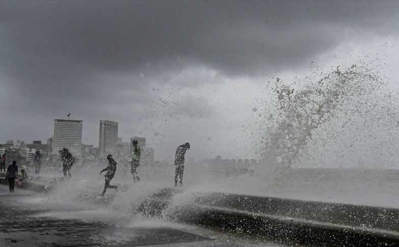 People visit the Marine Drive as sea waves crash on the shore during a high tide in Mumbai on Wednesday. (Image: PTI)